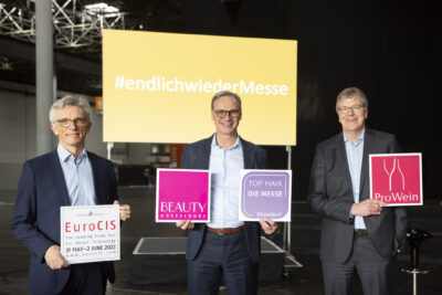 Three men hold colorful signs into the camera; copyright: Messe Düsseldorf