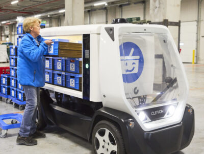 Eine Mitarbeiterin belädt ein autonomes Fahrzeug mit Kisten