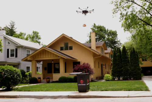 A drone ropes a package into a mailbox outside an apartment building