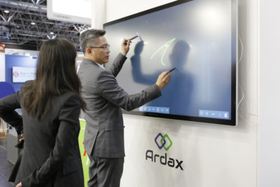 A man in a suit draws something on a touch screen