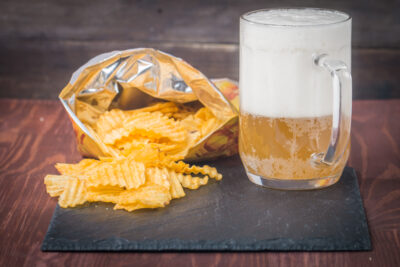 Beer with foam in glass mug and potato chips in bag on wooden table