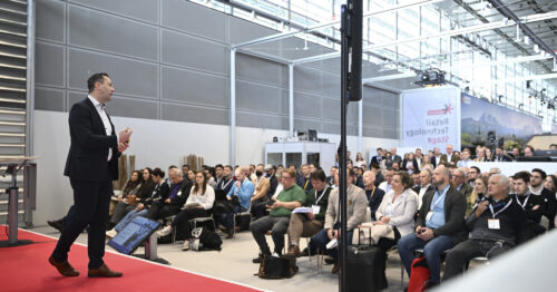 An audience during a presentation at a trade fair, left in the picture a speaker on a red stage