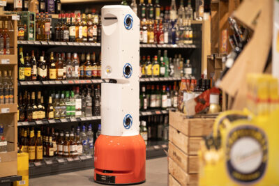 An inventory robot drives through a supermarket in front of a wine rack