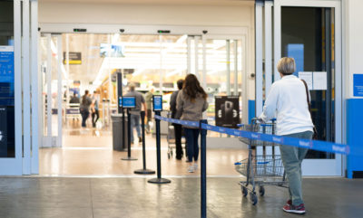 Customers stand in a queue in front of and in a store with a long distance between them