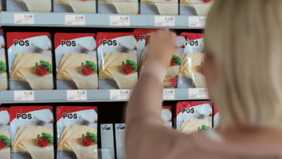 A woman grabs a product from a supermarket shelf, photographed from behind