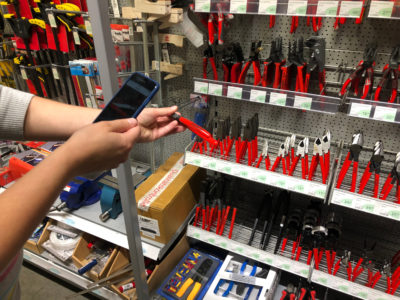 A person holds a smartphone in one hand and a pair of pliers with barcode in the other