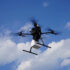 A drone carries a package through the air against a blue sky