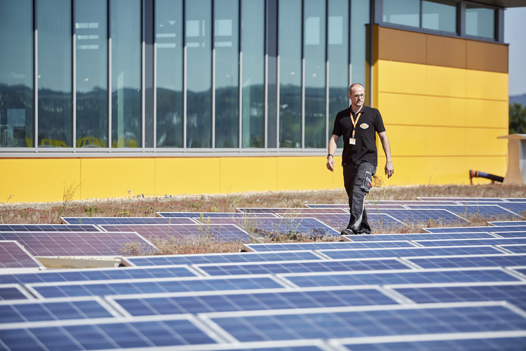Photovoltaikanlage auf dem Dach eines Globus. Ein Mitarbeiter von Globus läuft zwischen den Anlagen hindurch.