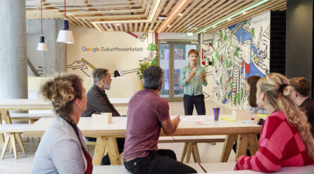 Mehrere Personen sitzen bei einem Workshop zusammen, im Hintergrund steht "Google Zukunftswerkstatt" an der Wand
