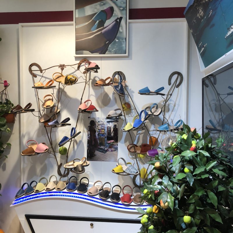 Warenpräsentation von Schuhen in einem Laden mit Sideboard und Metallgestänge, daneben ein grüner Plastikbaum, darüber ein Bild