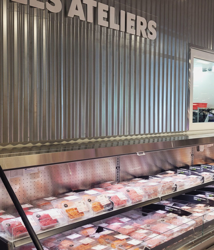 A meat cooling rack in front of a sheet metal wall in a louis delhaize OPEN MARKET