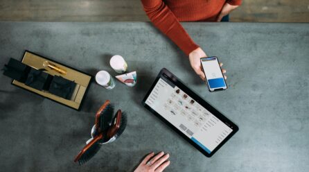 Several products and a tablet on a table and a person holding a smartphone; Copyright: Blake Wisz/Unsplash