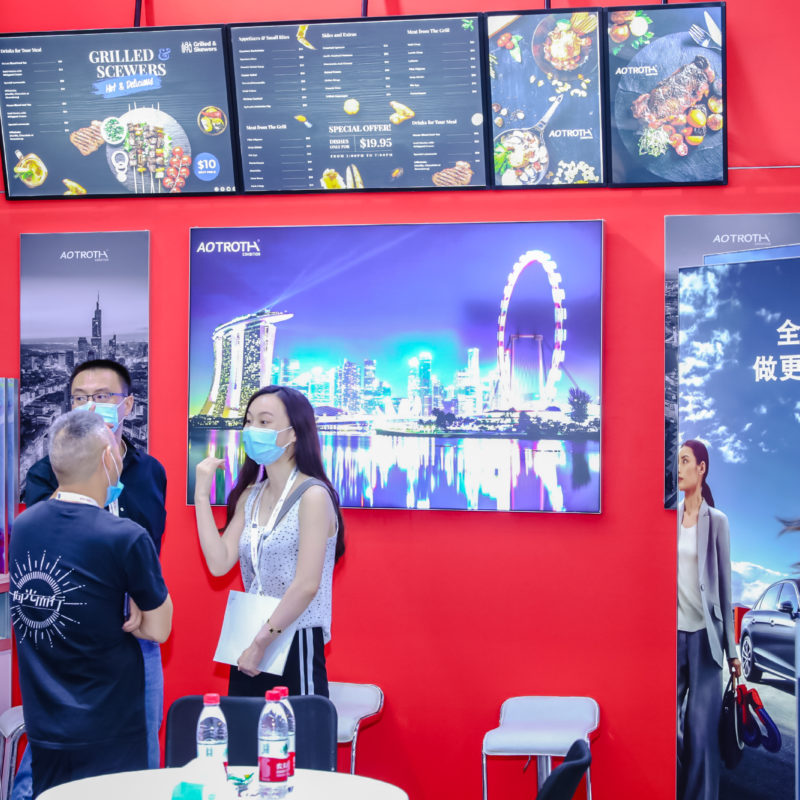 Two people stand at an exhibition stand with digital screens of different types