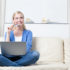A young blond woman sitting on a sofa with a laptop and a credit card