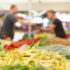 A man and a woman blurred in the background, hands stretched out to each other, vegetables in the foreground