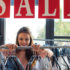 Woman looking at clothes on a hanger in front of a ‘sale’ sign; copyright: panthermedia.net / IgorVetushko