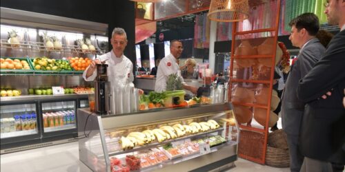 Two staff members stand at a refrigerated counter, in front of them visitors at a booth